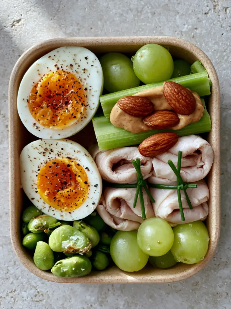 Healthy Road Trip Snacks: The Ultimate High-Protein Bento Box Guide 1 Close-up of healthy road trip snacks showing textures of cracked black pepper on jammy eggs and crisp celery.