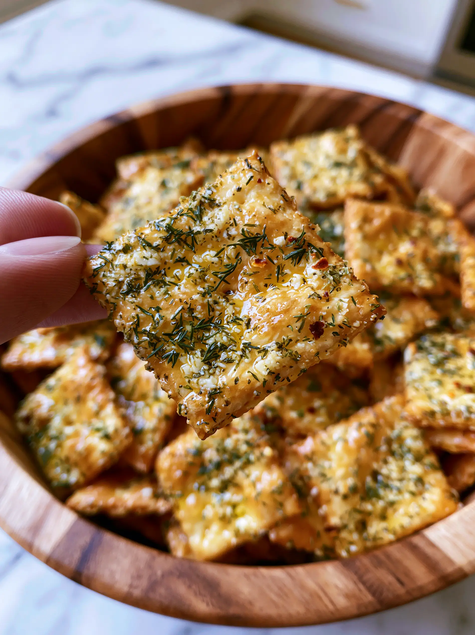 Dill Pickle Saltines: The Ultimate Zesty Ranch Snack Crackers 4 A macro shot of golden-brown Dill pickle saltines in a wooden bowl, glistening with oil and heavily encrusted with green dill weed and red pepper flakes.