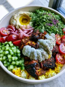 Close up shot of seared chicken thigh pieces with dark spice crust and thick white garlic sauce zig-zags. (chicken shawarma bowl)
