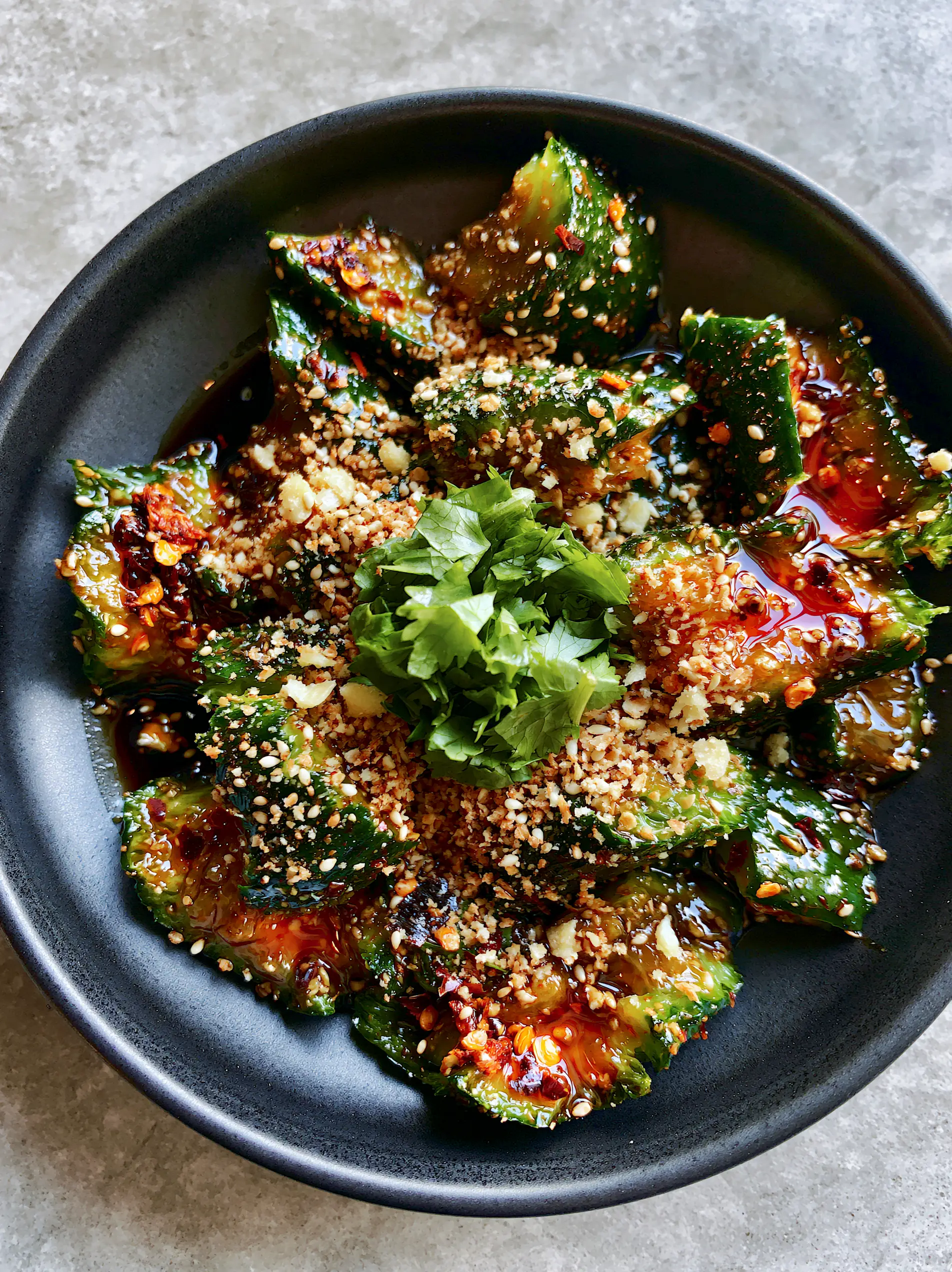 Asian Cucumber Salad Recipe: The Ultimate Smashed and Spicy Crunch 3 Top-down view of smashed Persian cucumbers with red chili flakes and sesame seeds in a minimalist matte black bowl. (Asian cucumber salad)