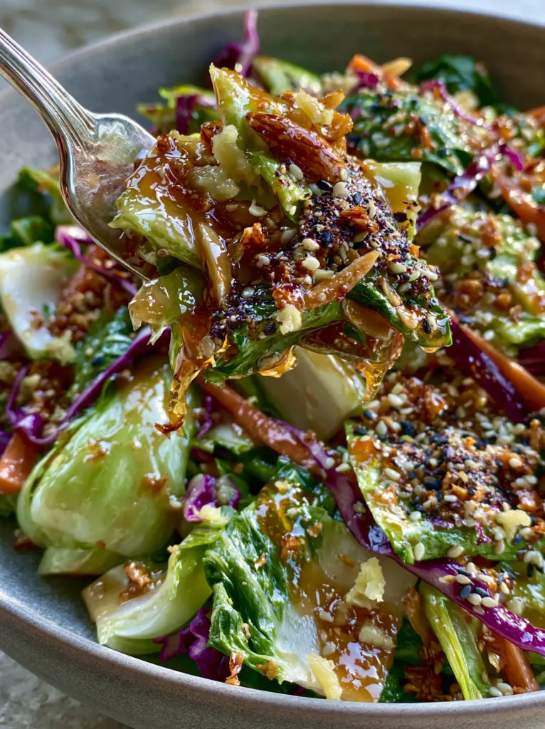 Macro texture of the glossy sesame ginger vinaigrette clinging to shredded cabbage and toasted almonds.