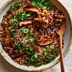Top-down view of a ceramic bowl containing mushrooms with sticky rice, garnished with green scallions and red chili. (mushrooms with sticky rice)