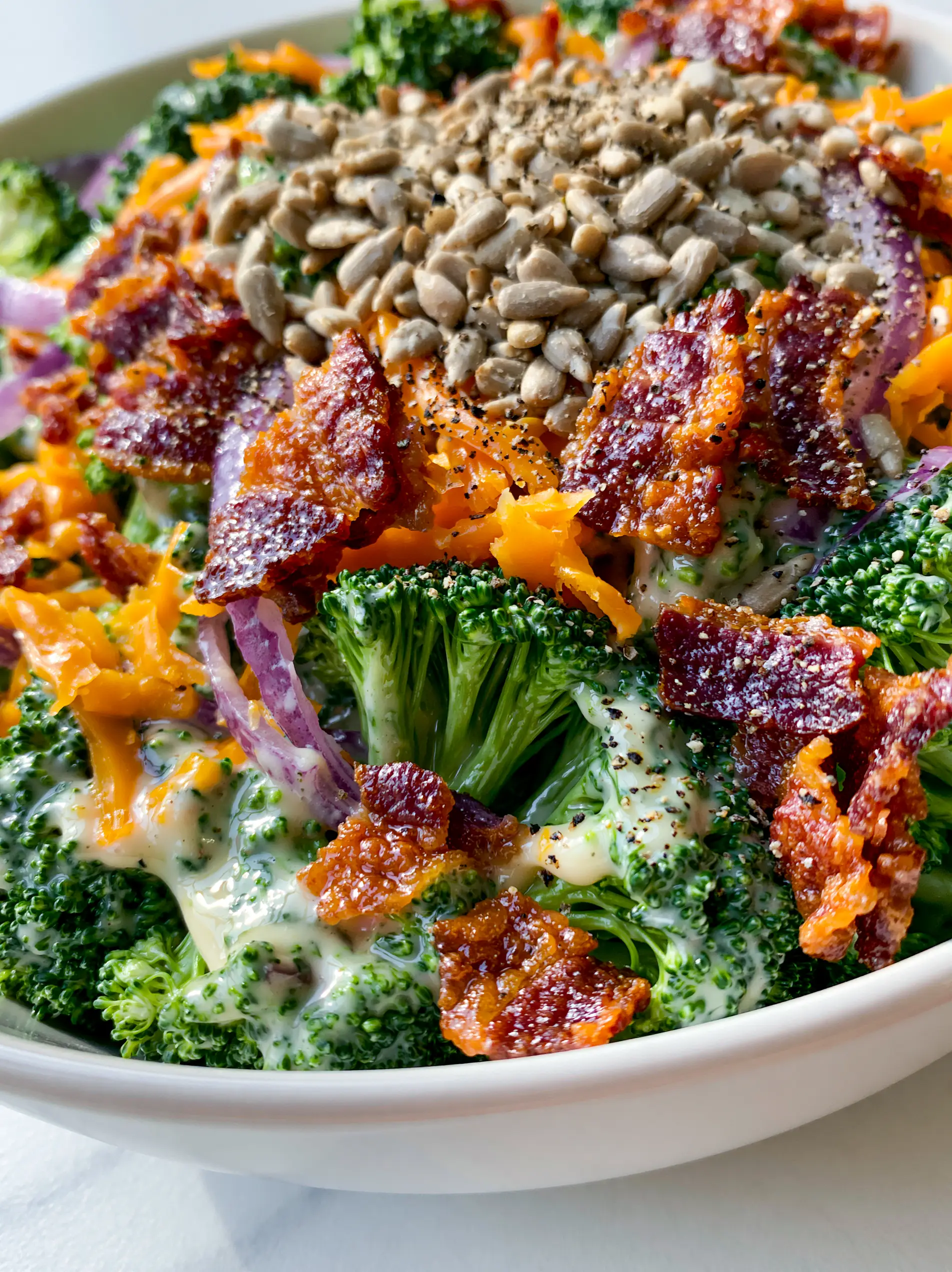 Extreme macro close-up of cold broccoli salad showing glossy dressing and cracked black pepper flakes.
