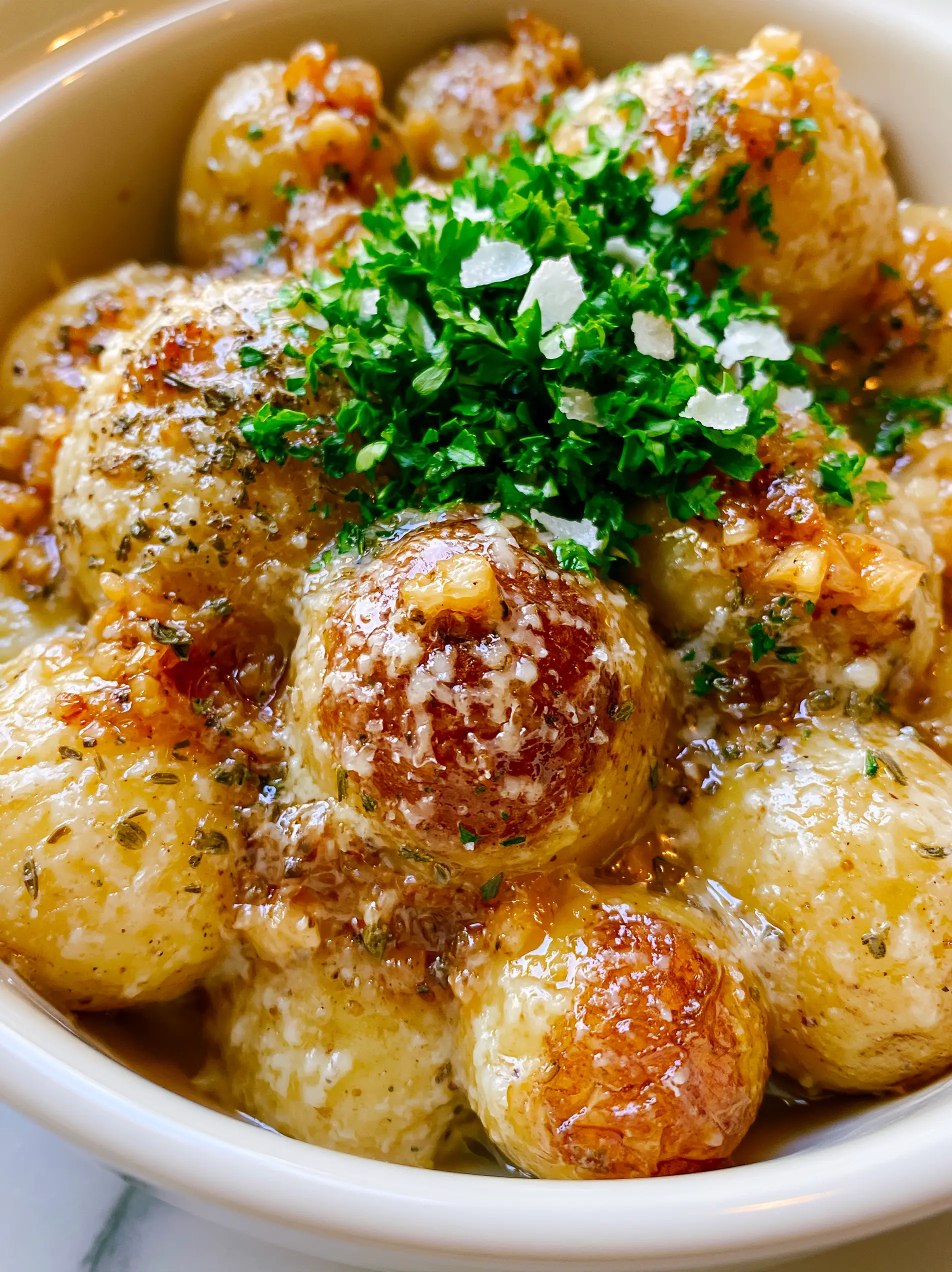 Slow Cooker Baby Potatoes with Garlic, Butter, and Parmesan 3 Overhead handheld photo of slow cooker baby potatoes with garlic, butter, and parsley in a white ceramic slow cooker.
