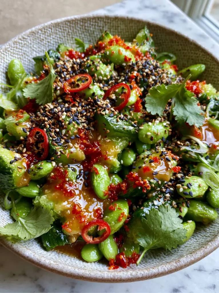 Cucumber Edamame Salad with Smashed Miso Ginger Dressing 2 Close-up of smashed Persian cucumbers and edamame coated in a glossy amber miso ginger dressing with visible red chili flakes.