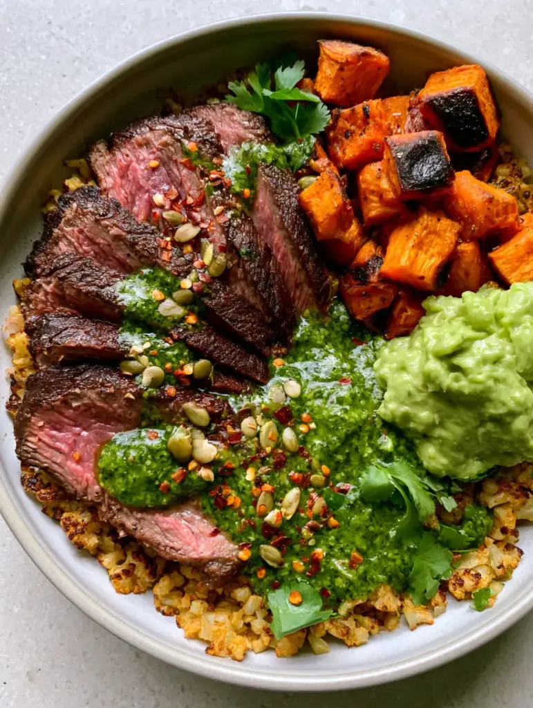 Overhead shot of a Paleo harvest bowl showing chimichurri drizzle and toasted pepitas.
