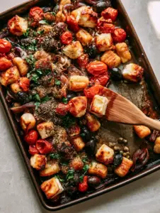 Top-down view of Greek Sheet Pan Gnocchi showing golden-brown toasted edges and bursting red cherry tomatoes.