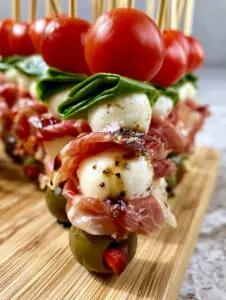 Close-up handheld photo of a bamboo skewer featuring prosciutto fat marbling and glistening balsamic glaze. (Graduation party appetizers)
