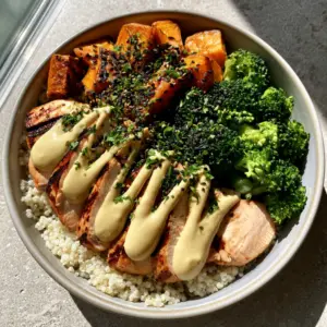 Top-down view of a ceramic bowl containing charred chicken breast, emerald broccoli, and sweet potato cubes over quinoa. (high protein bowl meals)