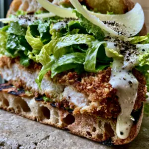 Extreme close-up of a halved Chicken Caesar Sandwich showing juicy chicken and panko crust.